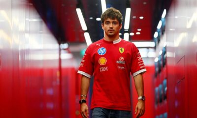 Charles Leclerc looking concerned in the Ferrari garage during a team strategy discussion at a Formula 1 race.
