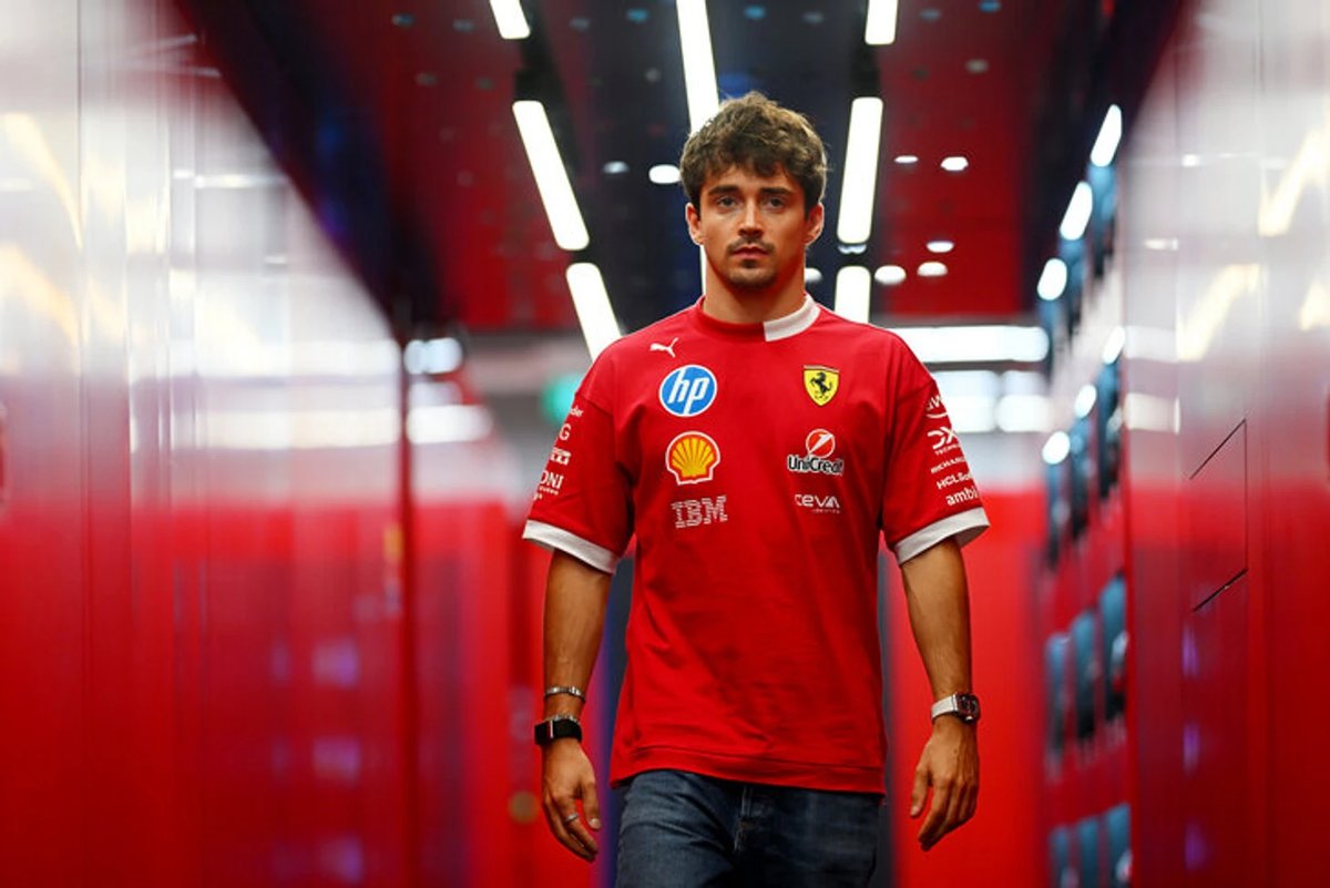 Charles Leclerc looking concerned in the Ferrari garage during a team strategy discussion at a Formula 1 race.