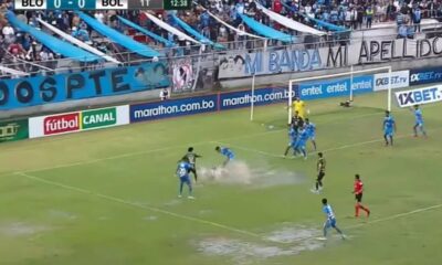 Chaotic Bolivian football match with referee showing a red card and players arguing on the pitch.