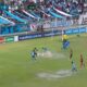 Chaotic Bolivian football match with referee showing a red card and players arguing on the pitch.