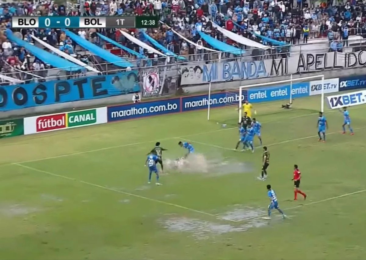 Chaotic Bolivian football match with referee showing a red card and players arguing on the pitch.