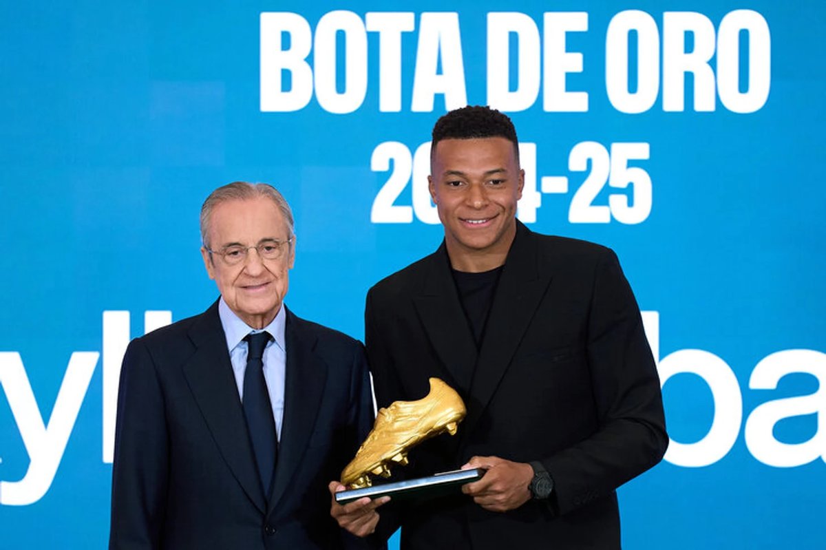 Kylian Mbappe holding the 2025 Golden Boot award on the pitch at Real Madrid's Santiago Bernabeu stadium.